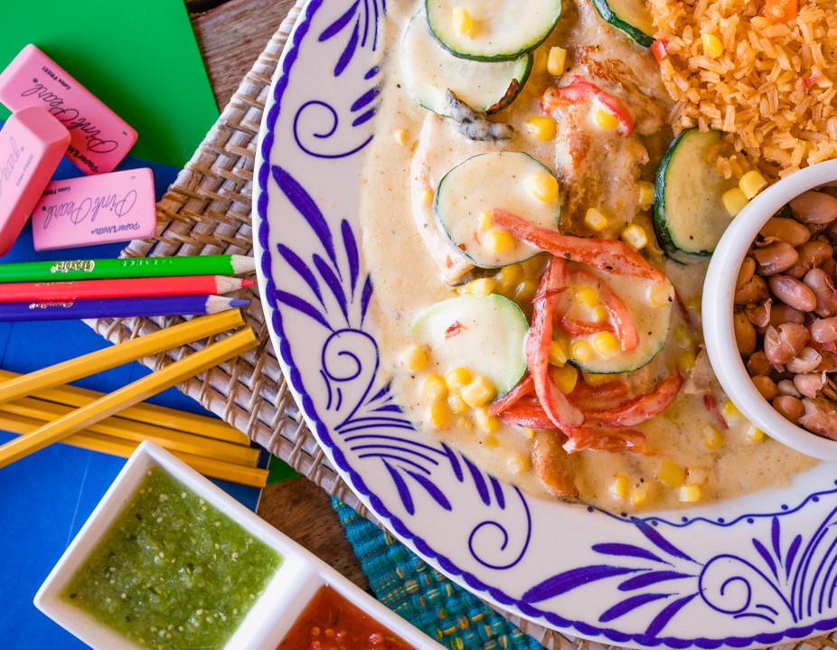 Various pencils and erasers next to plate of Pechuga con Calabaza